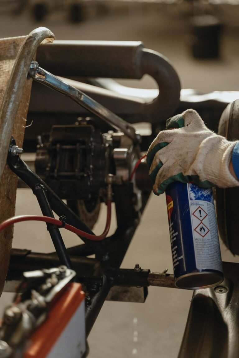 Close-up of a mechanic's glove holding lubricant spray while servicing a kart vehicle.